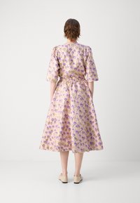 Abito floreale con motivi viola e gialli su sfondo rosa chiaro, maniche corte, vita aderente e gonna fluida.