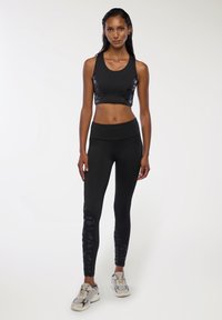 Czarny krótki top z błyszczącymi bocznymi panelami, w połączeniu z czarnymi legginsami o wysokim stanie z fakturowanymi akcentami i dopasowanym krojem. Fakturalne buty.