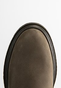 Bottine en daim marron avec un bout arrondi et une tige texturée. Elle est dotée d'une semelle en caoutchouc avec un accent noir le long du bord.