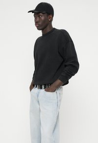 Černá mikina s kulatým výstřihem, světle modré džíny a černá čepice. Džíny mají volný střih; opasek má kulaté kovové doplňky.