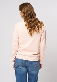 Světlé růžové svetr s žebrovanými manžetami a lemem, s volnějším střihem. Nošen s světle modrými, volně střiženými džínami. Měkká textura, jednoduchý design.