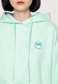 Miętowa bluza z kapturem wykonana z mieszanki bawełny, z przodem kieszeni, sznurkami i okrągłym logo z napisem "RINKO." Miękka w dotyku.