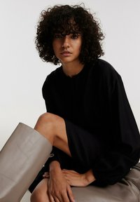 Schwarzes, übergroßes Kleid mit langen Ärmeln und rundem Halsausschnitt, kombiniert mit einem hellgrauen, glatten, knielangen Stiefel. Definierter strukturierter Stoff und klares Design.