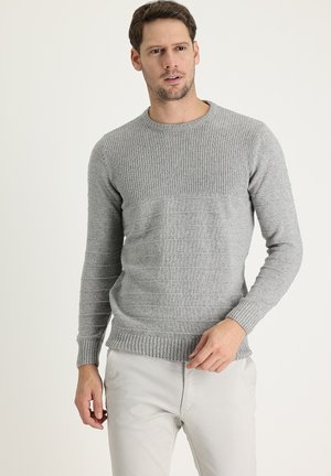 Suéter de punto gris con textura acanalada en los hombros y el dobladillo, que presenta un cuerpo liso y mangas largas, combinado con pantalones de color claro.