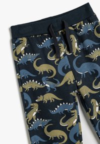 Joggers de algodón con un estampado de dinosaurios en azul y verde oliva sobre un fondo oscuro, con una cinturilla acanalada y detalles de cordón.