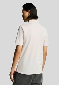 Lichtroze poloshirt met een kraag, korte mouwen en zijslits. Gemaakt van een gladde stof, met minimale ontwerpdetails.