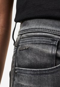 Vaqueros de denim en un lavado gris desgastado con corte ajustado. Cuenta con una etiqueta del logo de G-Star en el bolsillo trasero y detalles de costura visibles.