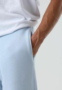 Lichtblauwe joggingbroek van zacht materiaal met een zijzak, gecombineerd met een wit T-shirt. De pasvorm oogt ontspannen en casual.