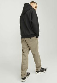 Sudadera con capucha negra, pantalones beige y zapatillas deportivas negras. La sudadera tiene un corte relajado; los pantalones cuentan con bolsillos laterales y un diseño ligeramente ajustado.
