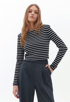 Zwart-wit gestreepte lange mouw top met een bootnek, gecombineerd met hoog getailleerde donkergrijze broek met plooien.