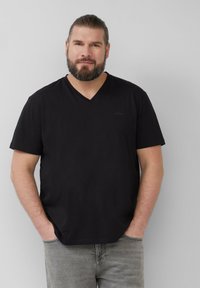 Czarny T-shirt z krótkim rękawem i dekoltem w serek o miękkiej fakturze, z małym logo na piersi, w połączeniu z jasnoszarymi dżinsami.