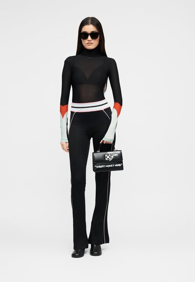 Γυναίκα που φοράει μαύρο διάφανο τοπ, μαύρο παντελόνι με λευκές και κόκκινες λεπτομέρειες, μαύρες μπότες, γυαλιά ηλίου, κρατώντας μαύρη τσάντα με λευκά γράμματα.