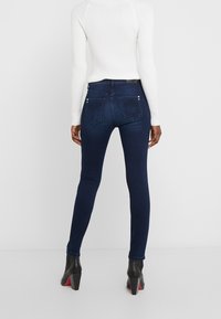 Jeans ajustados azul oscuro con una textura suave, que presentan bolsillos traseros y costuras decorativas, combinados con un suéter blanco de canalé y botas negras de tobillo.