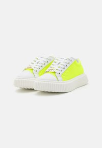 Baskets blanches et néon jaunes avec une tige en maille, un bout arrondi et une semelle en caoutchouc texturée ; elles disposent de lacets blancs et d'un petit accent doré.