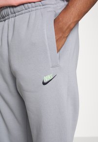 Pantalons de survêtement gris avec un tissu texturé, une taille élastique, des poches latérales et des logos Nike brodés en noir et vert fluo.