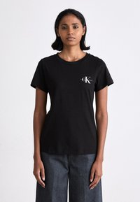 Black cotton t-shirt with a round neckline, short sleeves, and a white logo featuring the letters "CK" on the left chest area.