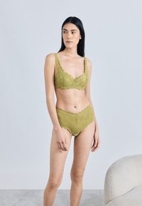 Pitsiline pesukomplekt oliivirohelises, millel on keerukad lillemustrid, lainelised servad ning laiad rihmad rinnahoidjal ja sobivad kõrge vöökohaga püksikud.