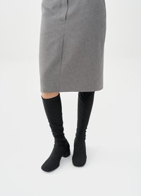 Μαύρες μπότες μέχρι το γόνατο με εφαρμοστό σχέδιο και υφή, σε συνδυασμό με γκρι pencil φούστα, που δείχνει ομαλό ύφασμα και κλασική κοπή.