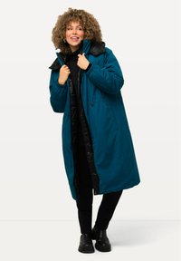 Tyrkysový dlouhý kabát s černým polstrovaným vnitřkem a límcem, s regulovatelným pasem, bočními kapsami a hladkým povrchem.