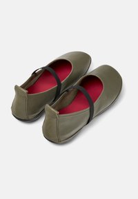 Mocasines de cuero verde oliva con puntera redonda y correa elástica negra, con un interior rojo brillante y un diseño de perfil bajo.