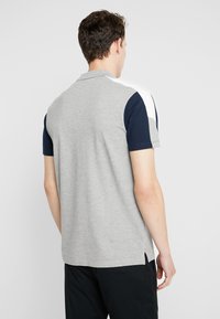 Šedá polokošile s krátkými tmavě modrými rukávy a bílým akcentem na ramenech. Boční rozparky pro komfort, s hladkou texturou.