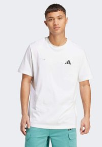 Hvid bomulds t-shirt med rund halsudskæring, korte ærmer og et sort Adidas-logo på brystet. Glat tekstur, afslappet pasform.