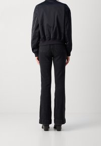 Námořnická bomber bunda s žebrovanými manžetami a spodním lemem, spárovaná s tmavými zvonovými džíny. Hladká textura látky s viditelnými švy a kapsami.