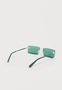Gafas de sol rectangulares sin montura con tinte verde, patillas delgadas de color verde oscuro y puente nasal de metal dorado sobre un fondo claro.