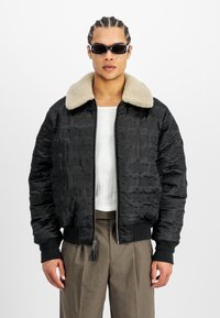 Chaqueta bomber acolchada negra con cuello de pelo sintético beige, cierre de cremallera y puños de canalé. Presenta patrones en relieve en la tela.