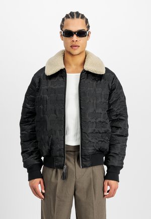 Zwarte gewatteerde bomberjack met een beige faux fur kraag, ritsclosure en gebreide manchetten. Bevat geperste patronen op de stof.