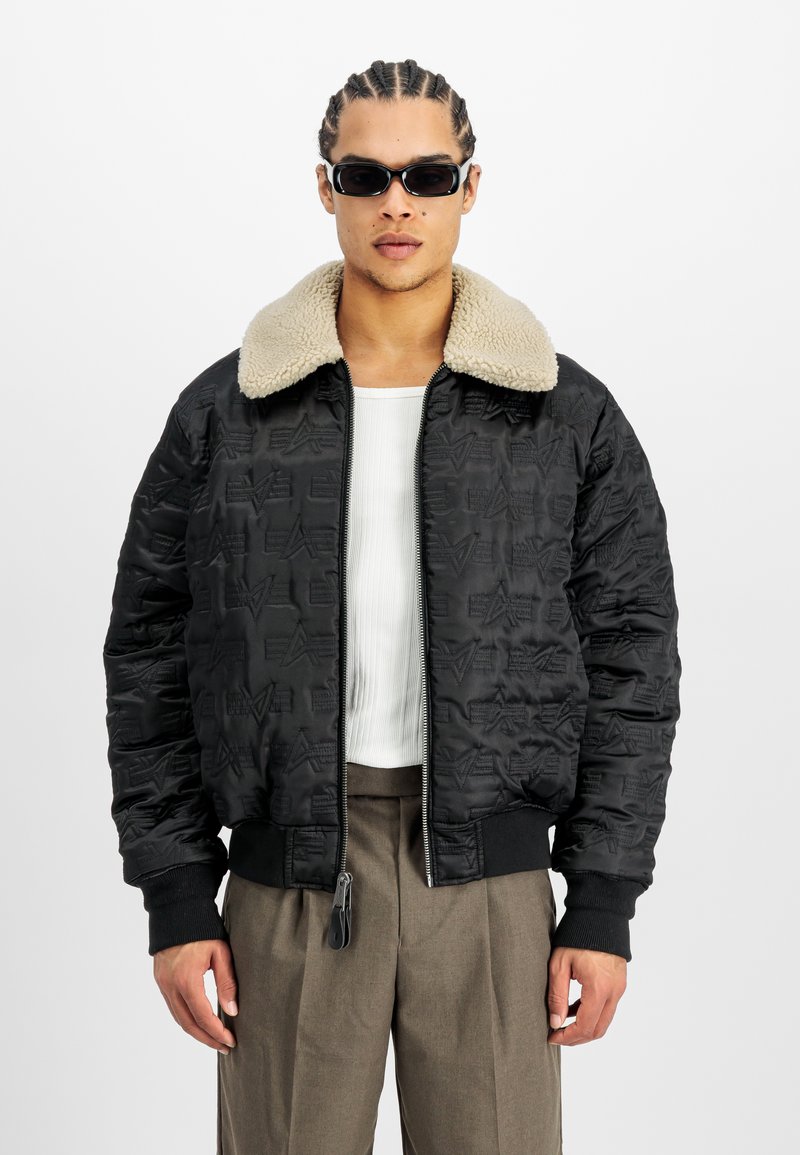 Chaqueta bomber acolchada negra con cuello de pelo sintético beige, cierre de cremallera y puños de canalé. Presenta patrones en relieve en la tela.