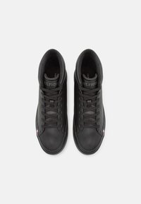 Zapatillas deportivas altas de cuero negro con cordones planos, cuello acolchado y suela de goma. Presentan un logo en la lengüeta y un acento en tres colores en el costado.