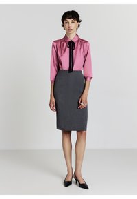 Blusa di raso rosa con cravatta nera e maniche tre quarti abbinata a una gonna a tubino grigia a righe. Tacchi a punta nera.