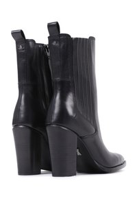 Bottines en cuir noir avec des côtés côtelés, des talons blocs hauts et des fermetures éclair à l'arrière. Fini lisse avec des tirettes pour faciliter l'enfilage.