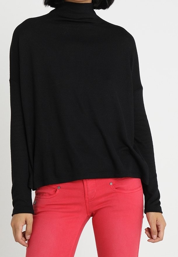 Pull à col roulé noir à manches longues, coupe décontractée, associé à un jean rose avec poches et détails de boutons. Texture en maille douce.