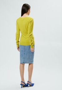 Maglione giallo a maniche lunghe, design aderente, abbinato a una gonna a tubino in denim azzurro e tacchi slingback blu, visto da dietro.
