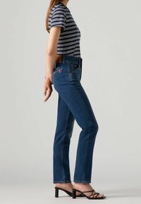 Jean en denim bleu avec une coupe droite, accompagné d'un haut à rayures à manches courtes et de sandales noires à talons. Présente un design minimaliste.