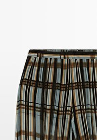 Plisseret nederdel med lodrette og vandrette striber i sorte, brune, beige og blå toner mod en hvid baggrund.