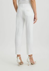 Pantalones rectos de mezclilla blanca con bolsillos traseros, cintura alta y un acabado texturizado. Llevados con sandalias blancas de tacón con correas en el tobillo.