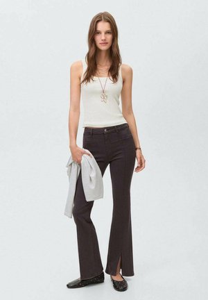 Hvid tank top, mørke flagrende jeans, grå cardigan i hånden, sorte flade sko med nitter, halskæde med blomst vedhæng. Glat stof, slim fit.