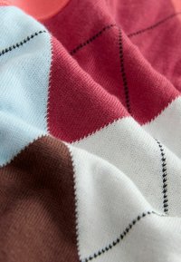 Tissu tricoté doux avec un motif losange en rouge, blanc, bleu clair et marron, montrant des coutures détaillées et une texture.