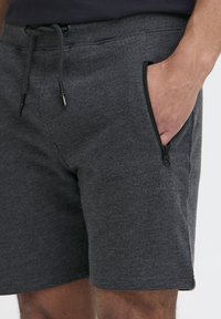 Dunkelgraue Shorts aus weichem Stoff mit einem Kordelzugbund und einer seitlichen Reißverschlusstasche. Glatte Textur ohne sichtbare Muster.