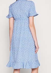 Hellblaues Blumenkleid mit kurzen Rüschensäumen, tailliertem Schnitt und weit auslaufendem Saum. Mit kleinen weißen Blumenmustern durchzogen.