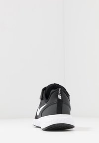 Zapato deportivo negro con parte superior sintética suave, swoosh blanco de Nike y correa de velcro. Cuenta con una media suela blanca texturizada y suela de goma.