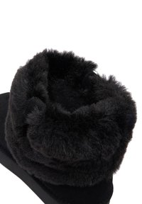 Sabot negru cu căptușeală din blăniță artificială, având o textură moale și pufoasă. Vârful este gros și rotunjit, completând designul elegant al corpului.