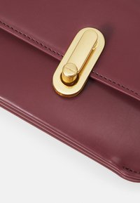 Borsa in pelle burgundy con superficie liscia, chiusura magnetica dorata e cuciture sottili lungo i bordi.