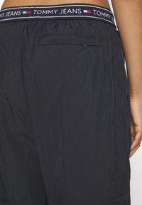 Czarne szorty Tommy Jeans z elastycznym paskiem w logo. Materiał wydaje się lekki i ma teksturowane wykończenie. Zawiera tylną kieszeń.