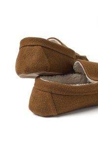 Pantofole in suede marrone con morbida fodera in pile, parte posteriore arrotondata e dettagli di cucitura minimalisti. La suola è piatta e testurizzata per una migliore presa.