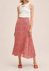 Jupe midi fleurie rouge avec une silhouette en ligne A et un tissu léger, associée à un haut blanc sans manches et des sandales rouges.