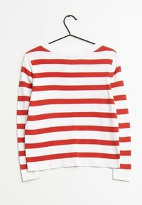Biały sweter w poziome czerwone paski, okrągły dekolt i długie rękawy. Wiszący na czarnym wieszaku na jednolitym tle.